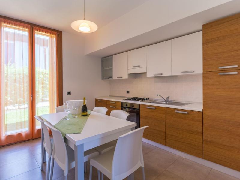 Modern eingerichtete Küche mit Esstisch, weißen Stühlen und Holzschränken neben einer großen Glastür.