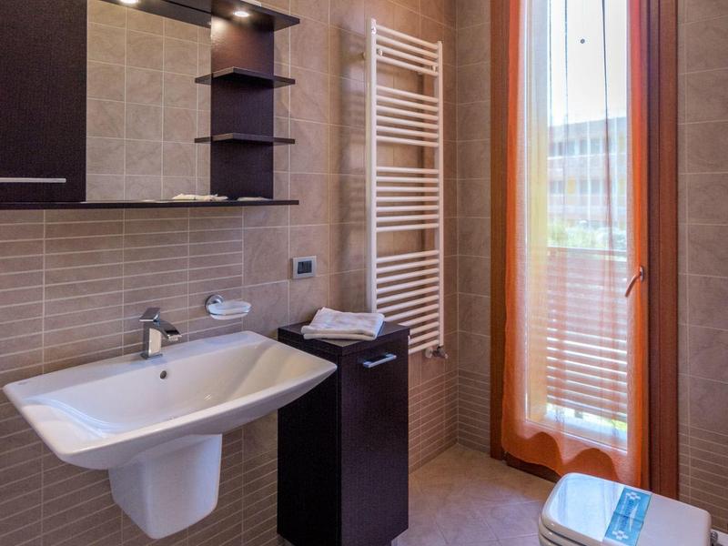 Modernes Badezimmer mit Waschbecken, Spiegel, Heizung und Bidet neben einer Glas-Tür mit orangefarbenem Vorhang.