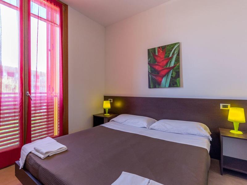 Modernes Hotelzimmer mit Doppelbett, brauner Bettdecke, gelben Lampen und rotem Vorhang am Fenster.