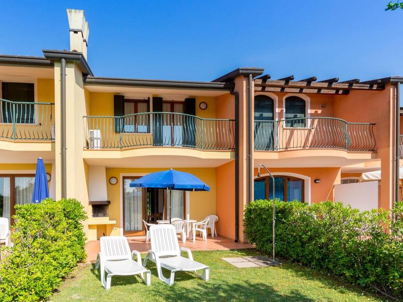 Reihenhaus mit Terrasse, Garten und Liegestühlen bei klarem Himmel.