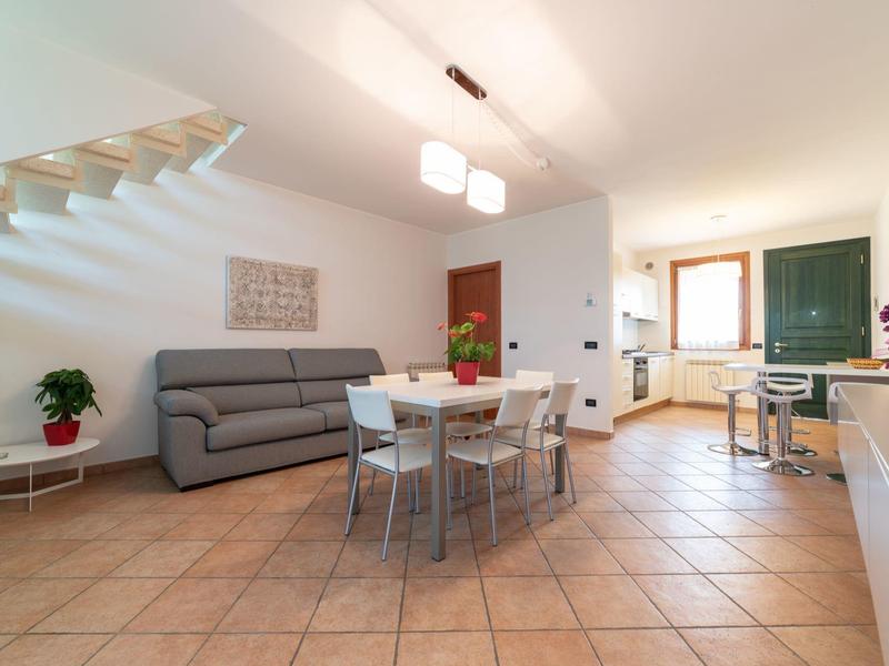 Helles Wohnzimmer mit grauem Sofa, Esstisch und moderner Küche in einem Ferienhaus.