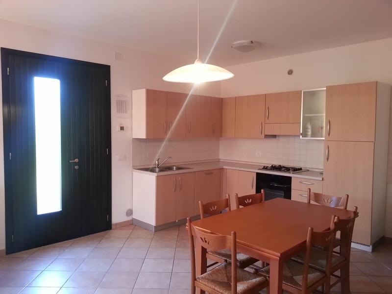 Helle Küche mit Holzmöbeln, Esstisch, Stühlen und großer Haustür mit Glasfenster.