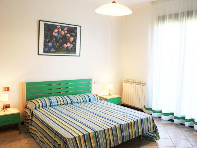 Hell eingerichtetes Schlafzimmer mit grünem Kopfteil, gestreiftem Bett und heller Gardine.