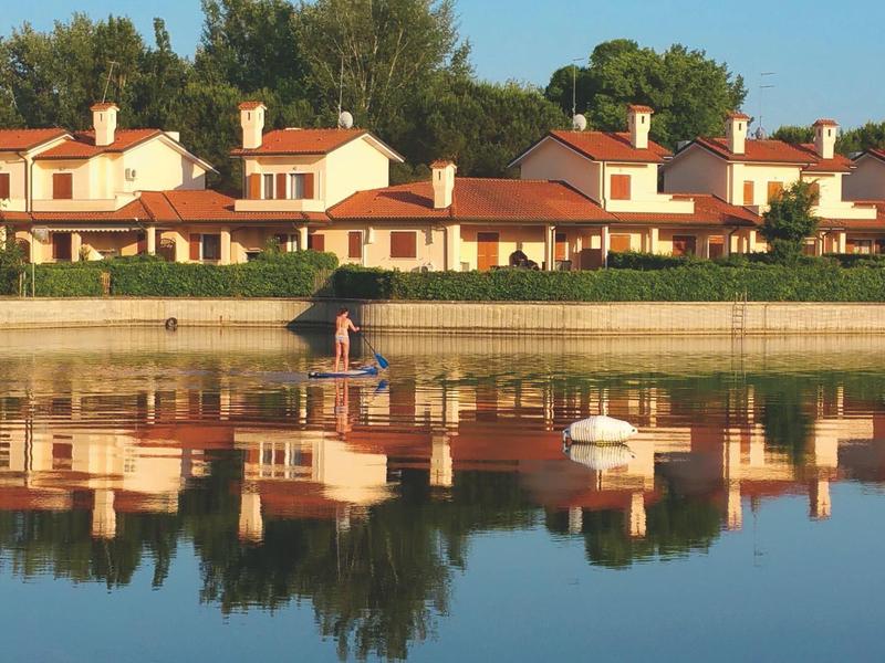 Reihe von Ferienhäusern mit roten Dächern am Ufer eines ruhigen Sees mit Spiegelungen im Wasser.
