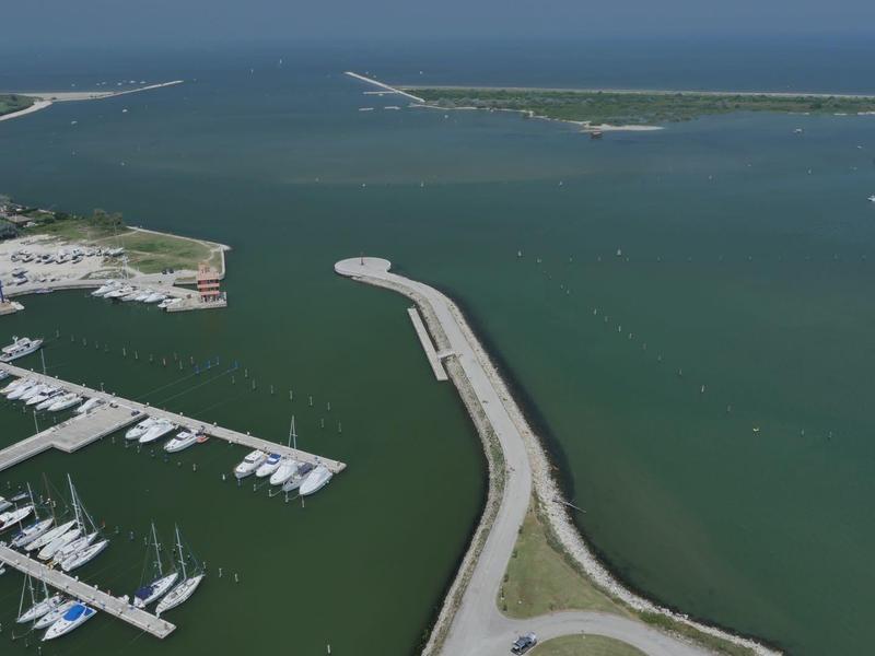 Luftaufnahme eines Hafens mit Yachten und einem langen Pier, umgeben von Wasser.