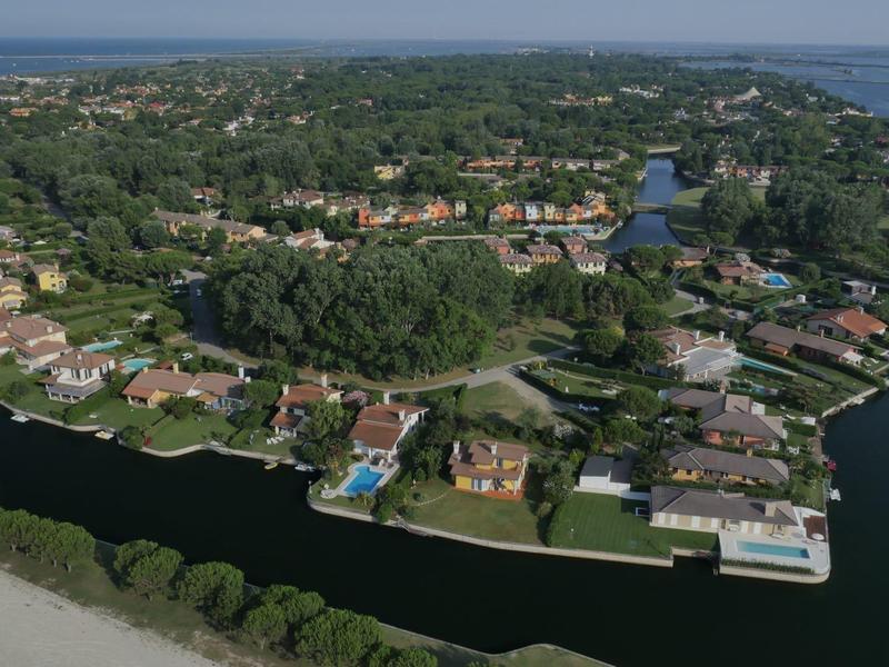 Luftaufnahme einer Halbinsel mit Wohnhäusern, Wasserkanälen und einem Strand im Vordergrund.