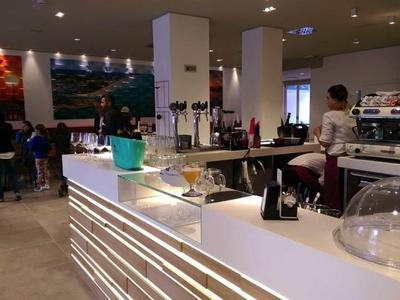 Moderner Café-Innenraum mit weißer Theke, LED-Beleuchtung, Kaffeekapseln und Mitarbeitern im Hintergrund.