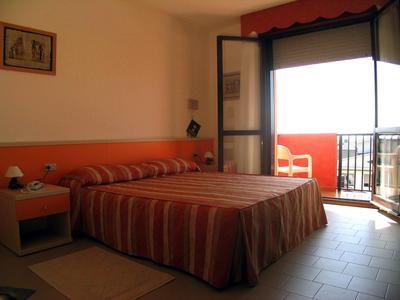 Einfaches Hotelzimmer mit Doppelbett, rot gestreifter Bettdecke, Nachttisch und Balkon mit Ausblick.