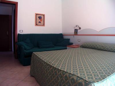 Schlafzimmer mit großem Bett, grünem Sofa, Nachttisch und Wandbild, weiße Wände.