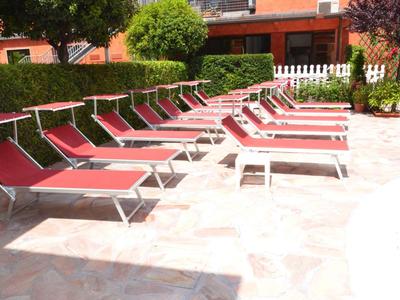 Mehrere rote Liegestühle neben einem Pool auf einer sonnigen Terrasse mit grünen Hecken.