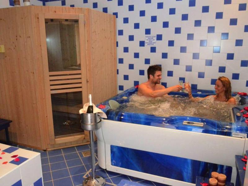 Ein Mann und eine Frau sitzen im blauen Whirlpool, daneben steht eine Holzkabine mit Glastür.
