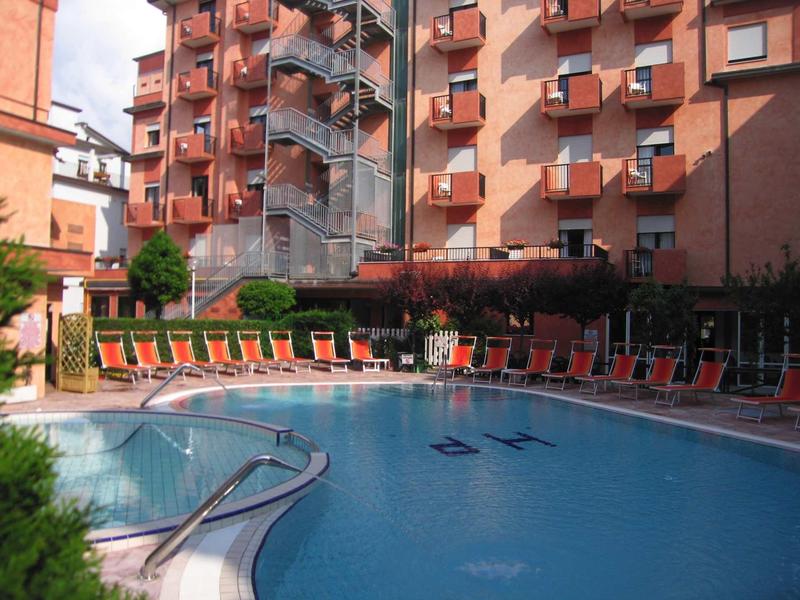 Ein runder Außenpool mit roten Liegestühlen und einem Stahltreppenturm an rotem Gebäude.