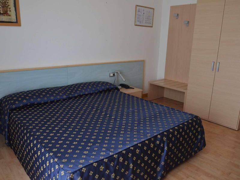 Ein kleines Schlafzimmer mit Doppelbett, blauem Bettbezug und hellem Holzschrank und Tisch.