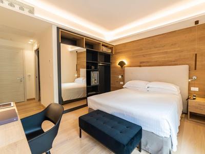 Helles Schlafzimmer mit Holzwand, weißem Bett, schwarzem Sitzbank und offenem Kleiderschrank.