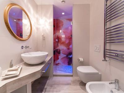 Modernes Badezimmer mit rundem Spiegel, Waschbecken, Toilette und Glasdusche mit farbigem Muster.