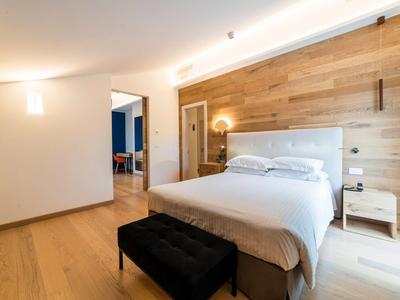 Helles Schlafzimmer mit Holzwand, großem Bett, schwarzer Bank und weißen Nachttischen.