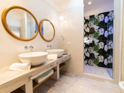 Modernes Badezimmer mit zwei runden Spiegeln, weißen Waschbecken und tropisch gemusterter Duschwand.