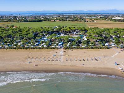 Vue aérienne d'une plage avec des rangées de parasols et des terres vertes avec des maisons derrière.