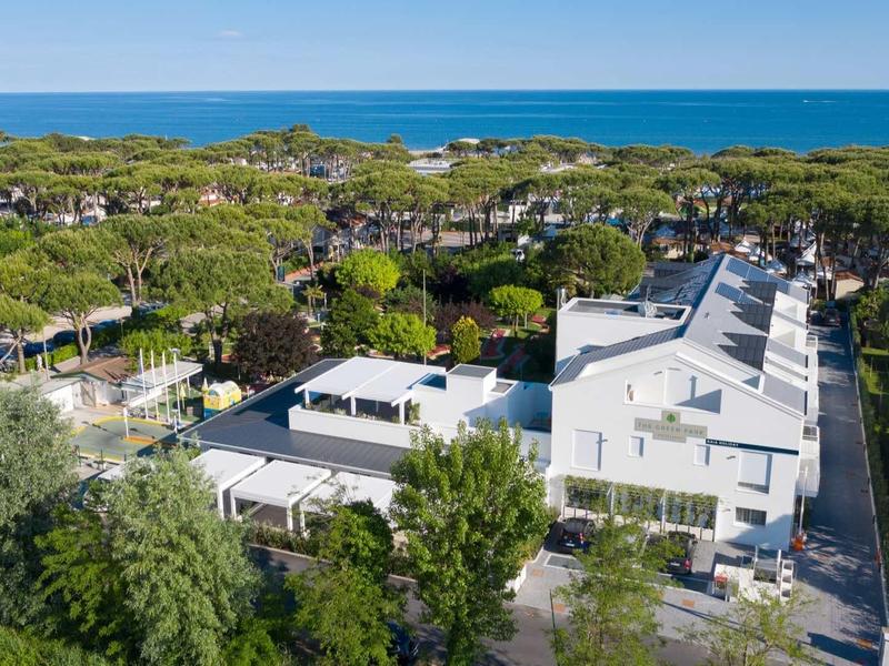 Moderne weiße Gebäude mit Flachdach, umgeben von Bäumen und grüner Landschaft nahe dem blauen Meer.