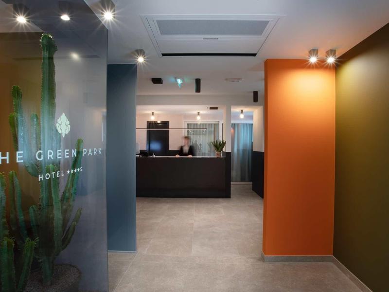 Moderner Hotel-Eingang mit Glaswand, Rezeption, grauem Boden und oranger sowie grüner Wand.
