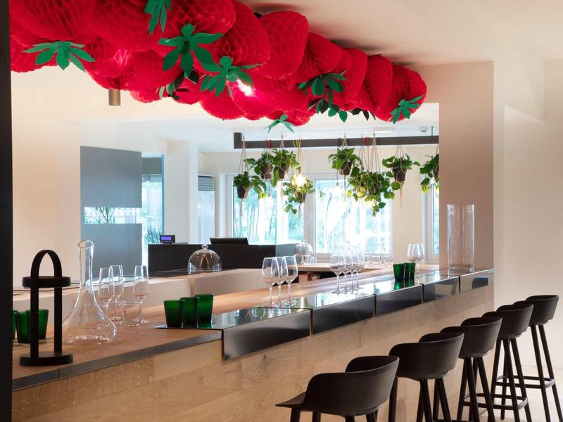 Moderner Tresen mit Holzfront, schwarzen Barhockern und roten, dekorativen Tomaten an der Decke.