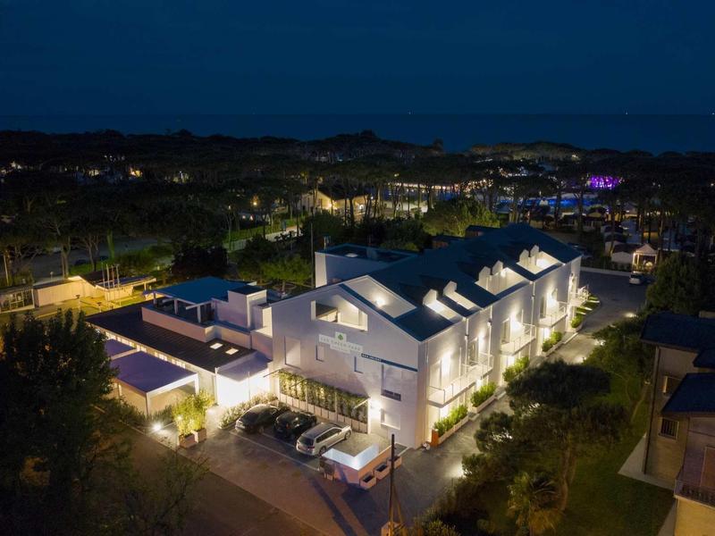 Moderner, beleuchteter Gebäudekomplex bei Nacht, umgeben von Bäumen und dunklem Himmel.