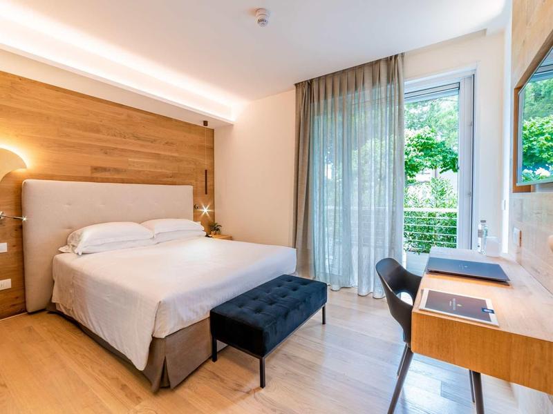 Modernes Schlafzimmer mit großem Bett, Holzvertäfelung, Schreibtisch und Zugang zum Garten.