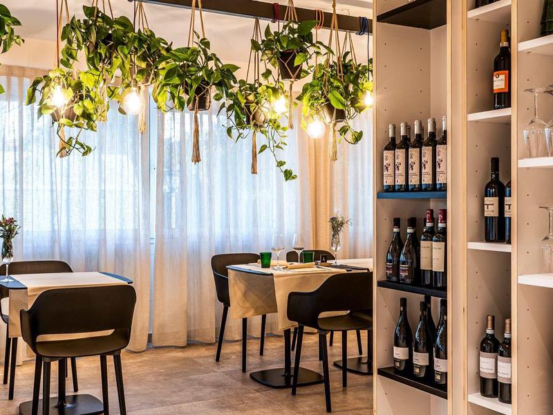 Modernes Restaurant mit hängenden Pflanzen, warmem Licht und Weinregalen aus Holz und Glas.