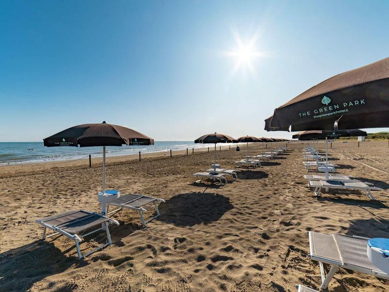 Strand mit Sand, leerem Liegestuhl, Sonnenschirmen und blauem Himmel bei Sonnenschein.