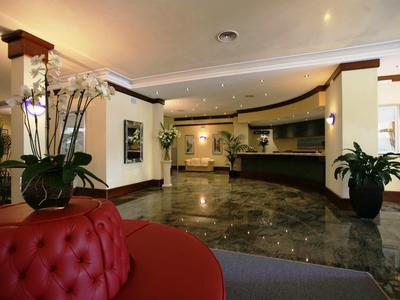 Jasny hol hotelowy z czerwonym sofą, marmurową podłogą i recepcją w tle.