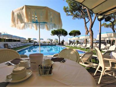 Terrassenblick mit gedecktem Tisch, Sonnenschirm, Pool und Bäumen bei sonnigem Wetter.