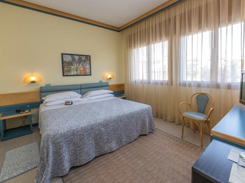 A bright, cozy hotel room with a double bed, desk, and TV.