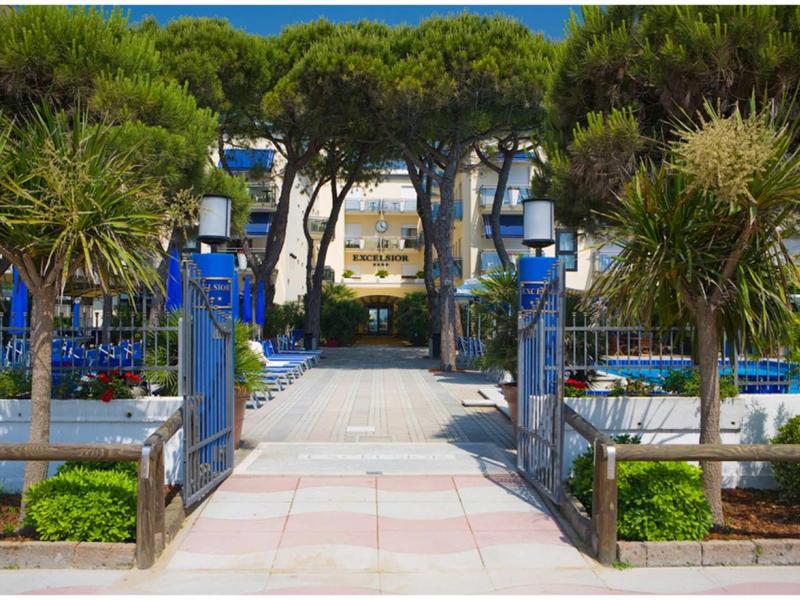 Wide path with blue and white lamps leads to a hotel, surrounded by palm trees and greenery.