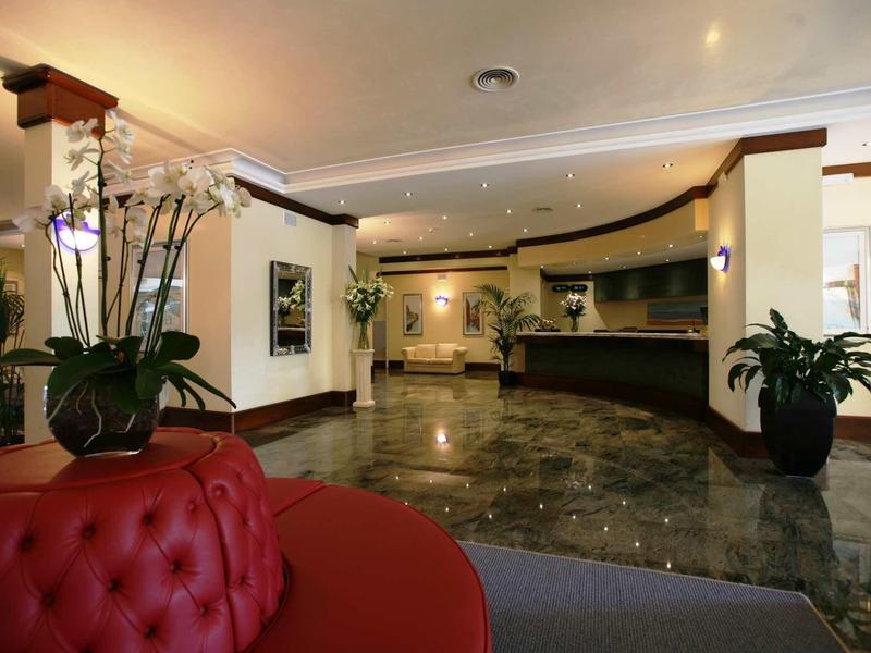 Elegant hotel lobby with red sofa, plants, and stone-colored flooring.