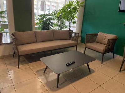 Moderner Wartebereich mit brauner Couch, Sessel, schwarzem Tisch und grünem Hintergrund.