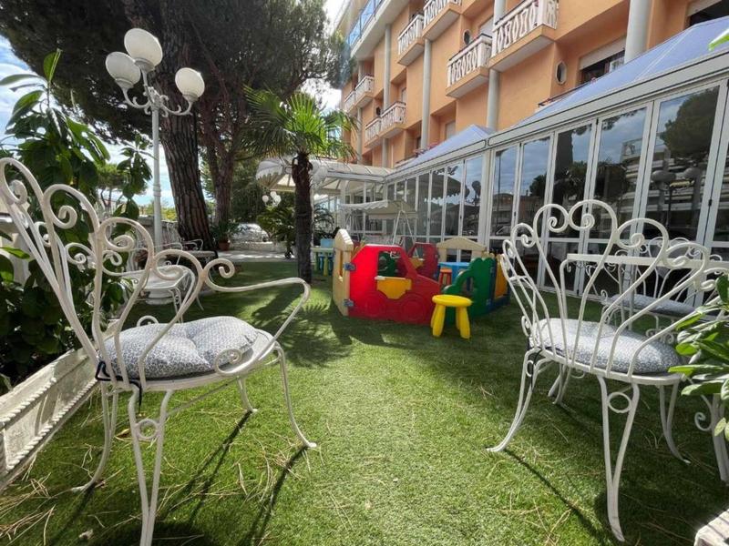 Jardin d'hôtel avec chaises métalliques blanches, maison de jeux pour enfants et chaise en plastique sur pelouse verte