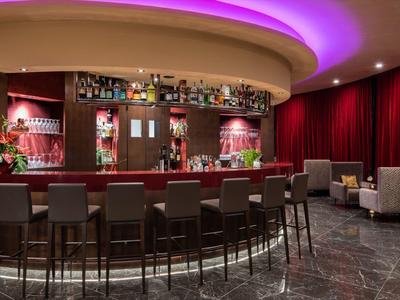 Elegante Hotelbar mit runden Theken, Barhockern und rotem Beleuchtungshintergrund