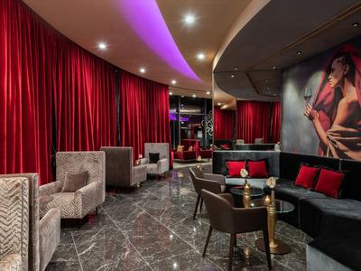 Moderne Lounge mit roten Vorhängen, grauen Sesseln, schwarzem Sofa und gedämpfter Beleuchtung.