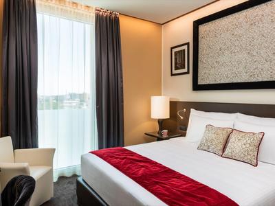 Modernes Hotelzimmer mit Doppelbett, roten Akzenten und großem Fenster mit Vorhängen.