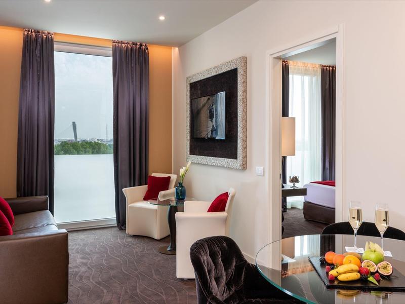 Modernes Hotelzimmer mit Sitzbereich, Flachbildfernseher und Blick auf den See durch das Fenster.