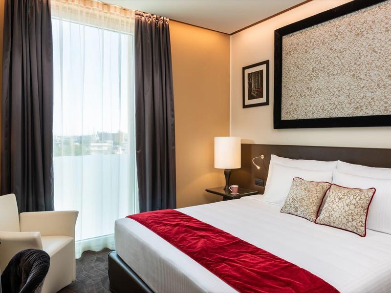 Modernes Hotelzimmer mit Doppelbett, roten Akzenten und großem Fenster mit Vorhängen.