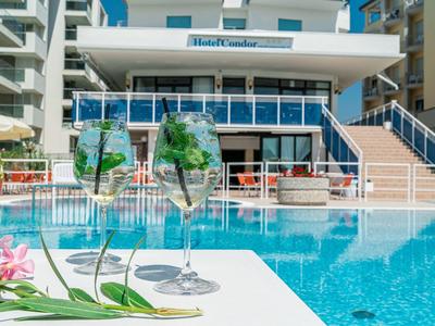 Due bicchieri di vino accanto a una piscina con edificio dell'hotel sullo sfondo.