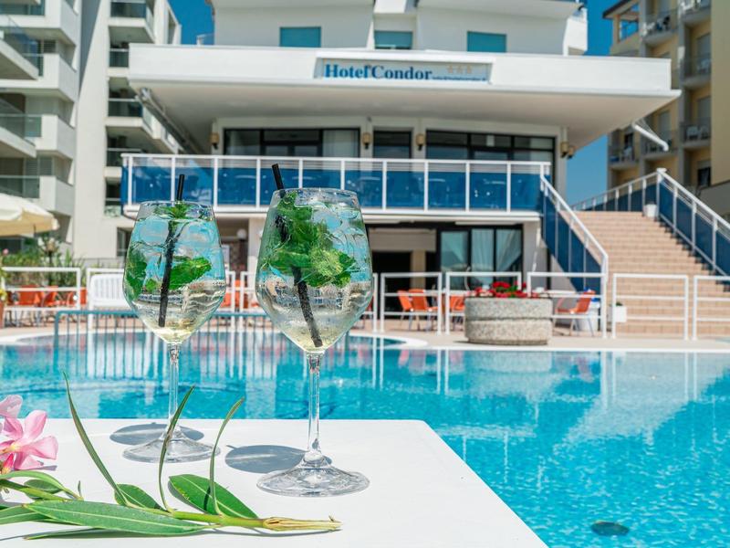 Due bicchieri di vino accanto a una piscina con edificio dell'hotel sullo sfondo.