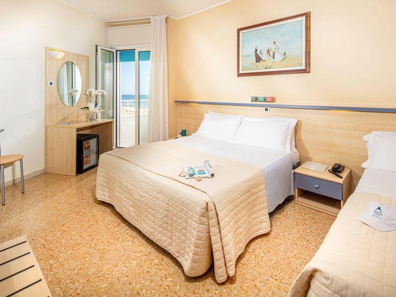 Camera d'hotel con due letti, comodino, sedia e balcone con vista mare