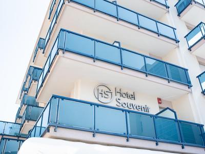 Widok białego budynku hotelowego z niebieskimi balkonami i napisem Hotel Souvenir.