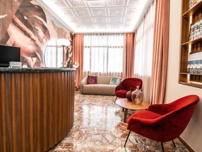 Jasna lobby hotelowa z czerwonym fotelem, recepcją i dużą dekoracją ściany przy oknie