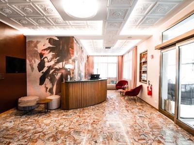 Jasna lobby hotelowa z brązowym recepcją, beżowymi ścianami i czerwonym fotelem.