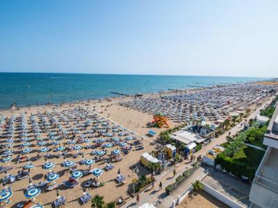 Widok na zatłoczoną piaszczystą plażę z licznymi parasolami i leżakami nad morzem.