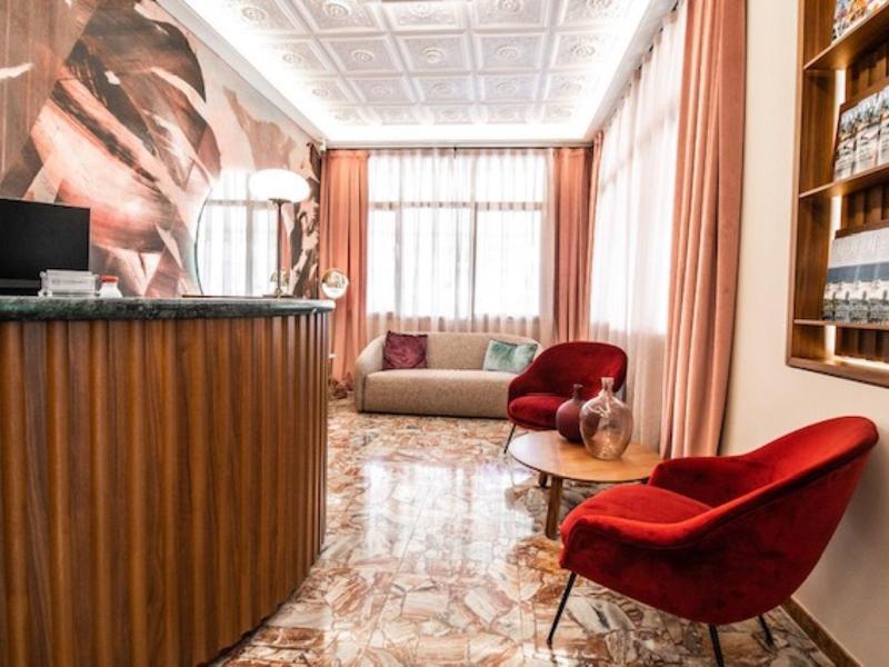 Jasna lobby hotelowa z czerwonym fotelem, recepcją i dużą dekoracją ściany przy oknie