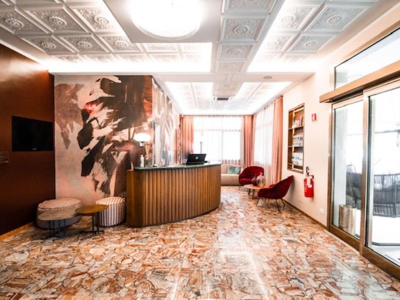 Jasna lobby hotelowa z brązowym recepcją, beżowymi ścianami i czerwonym fotelem.